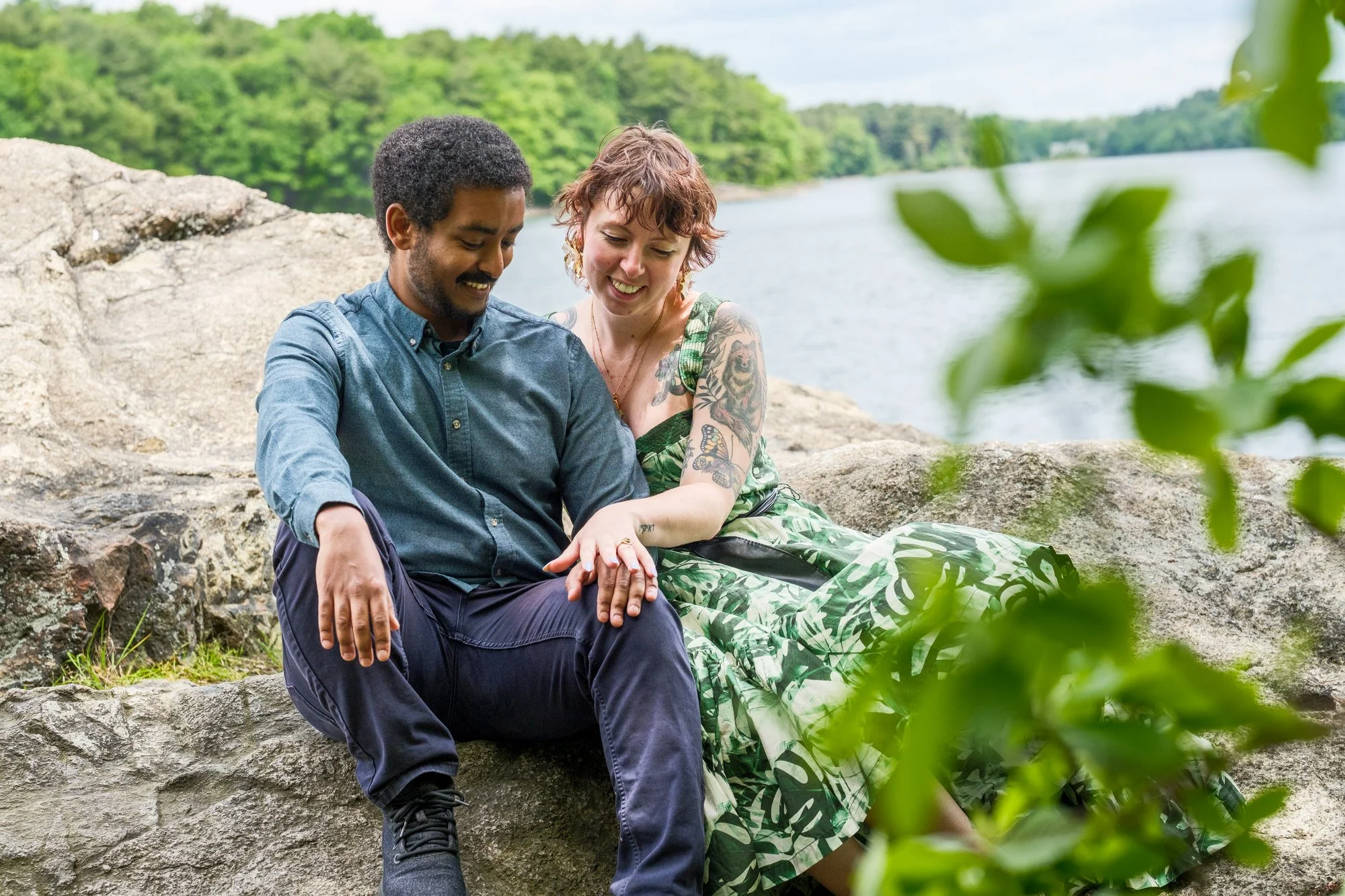 Couple sitting on rocks by the water for engagement portraits at Middlesex Fells