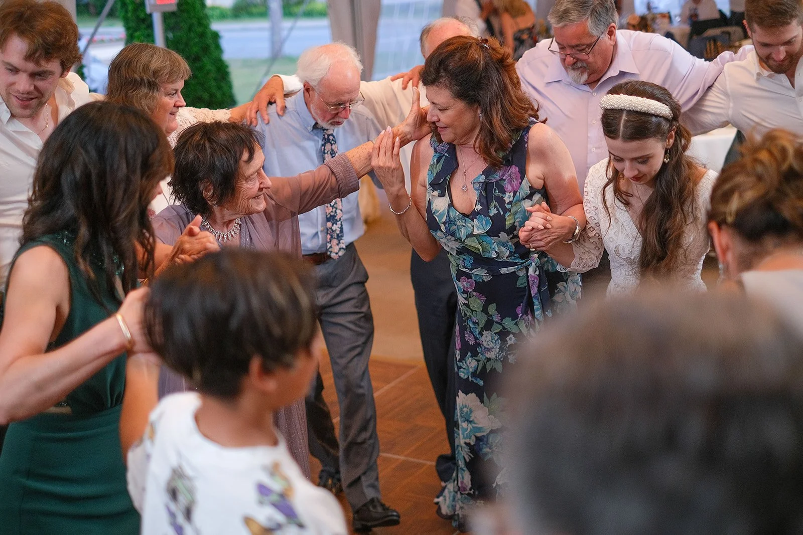 Group of people dancing in a circle, holding hands, at a celebration or party.