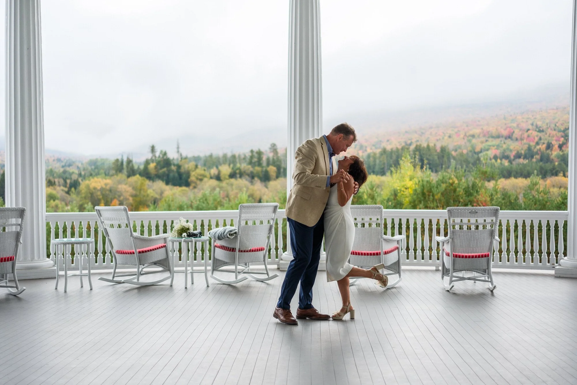 A couple dancing on the balcony of the Mount Washington Hotel with the fall foliage in the background