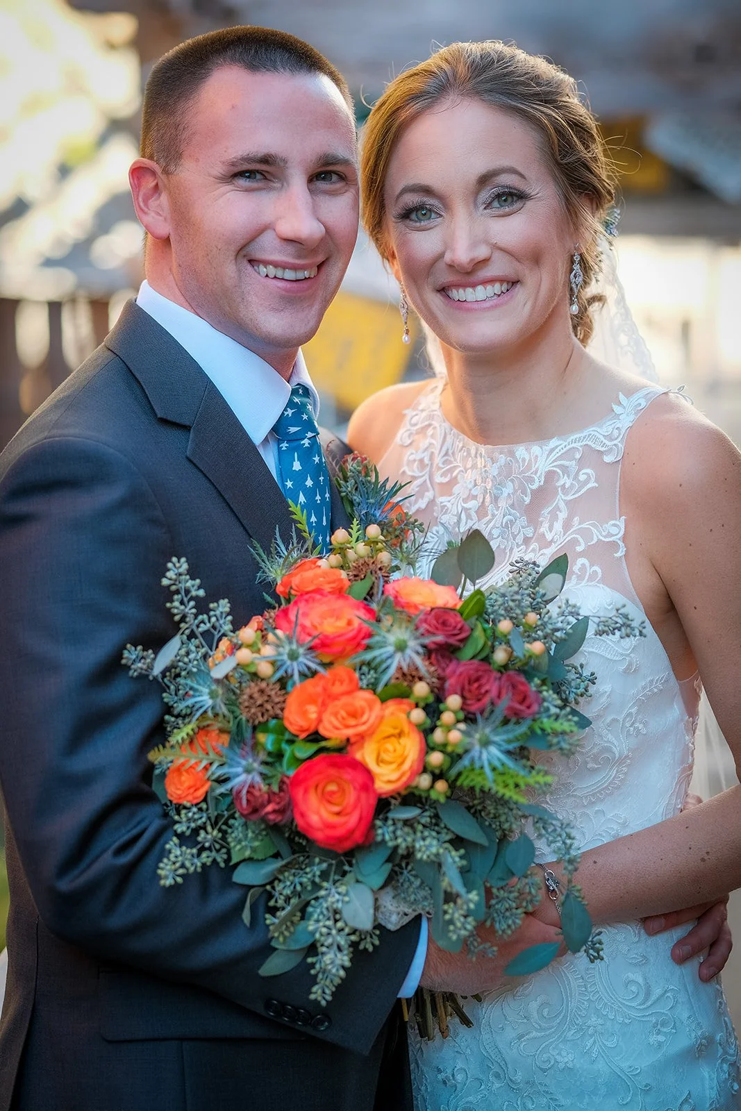 A newlywed couple smiling at the camera during their wedding, holding a colorful bouquet of flowers.