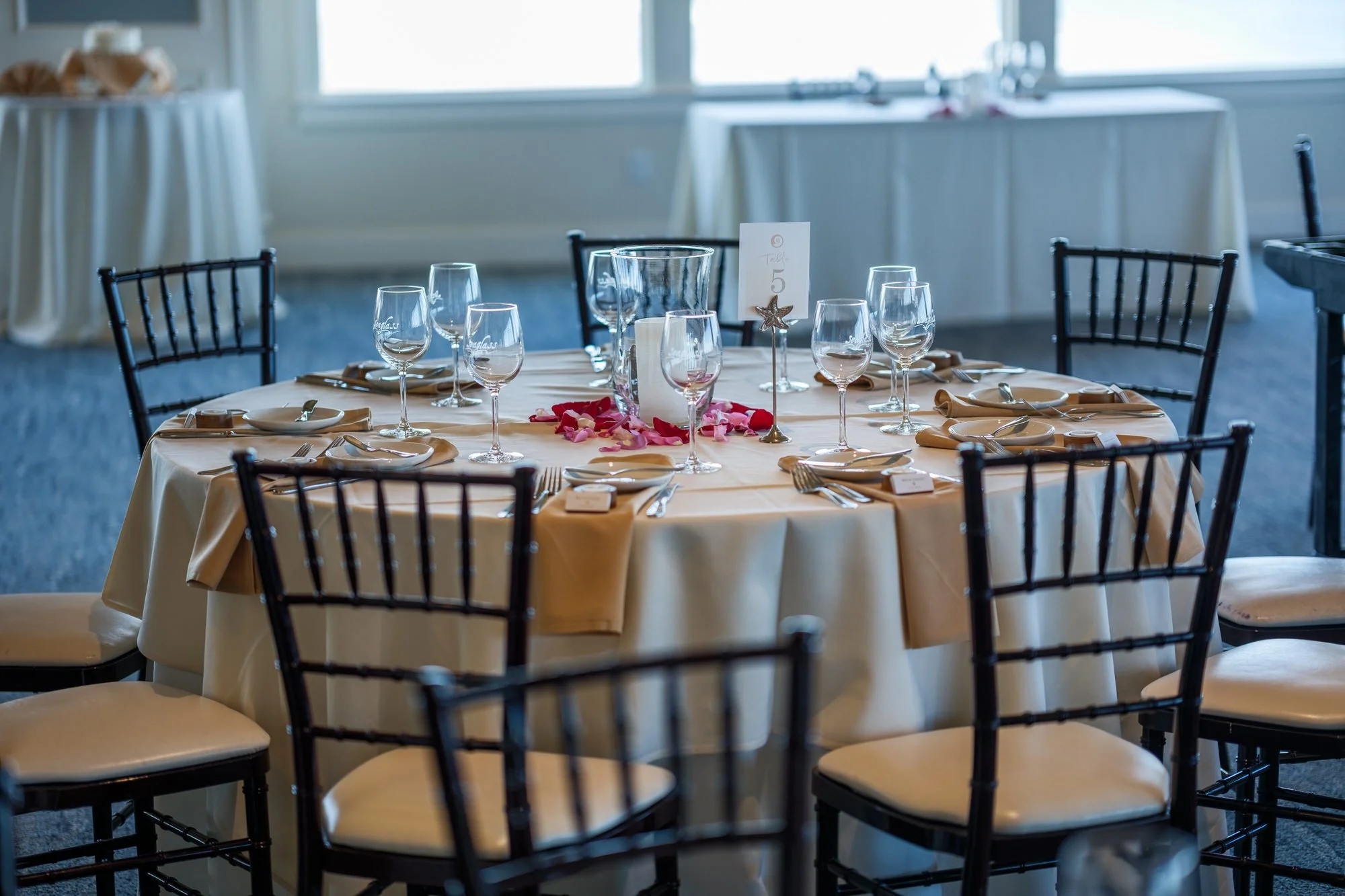 Reception table setting with glassware and rose petals at Blue Ocean Event Center.