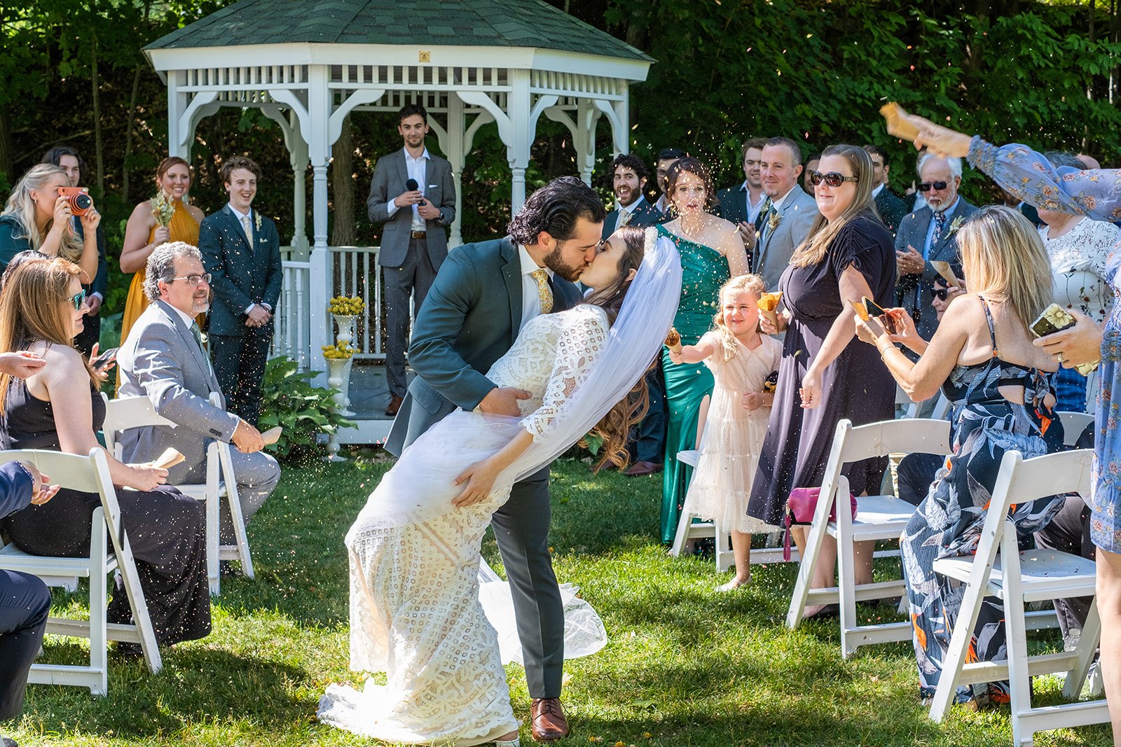 Groom dipping bride for a kiss during recessional at The Wentworth Inn gazebo as guests toss confetti in Jackson NH