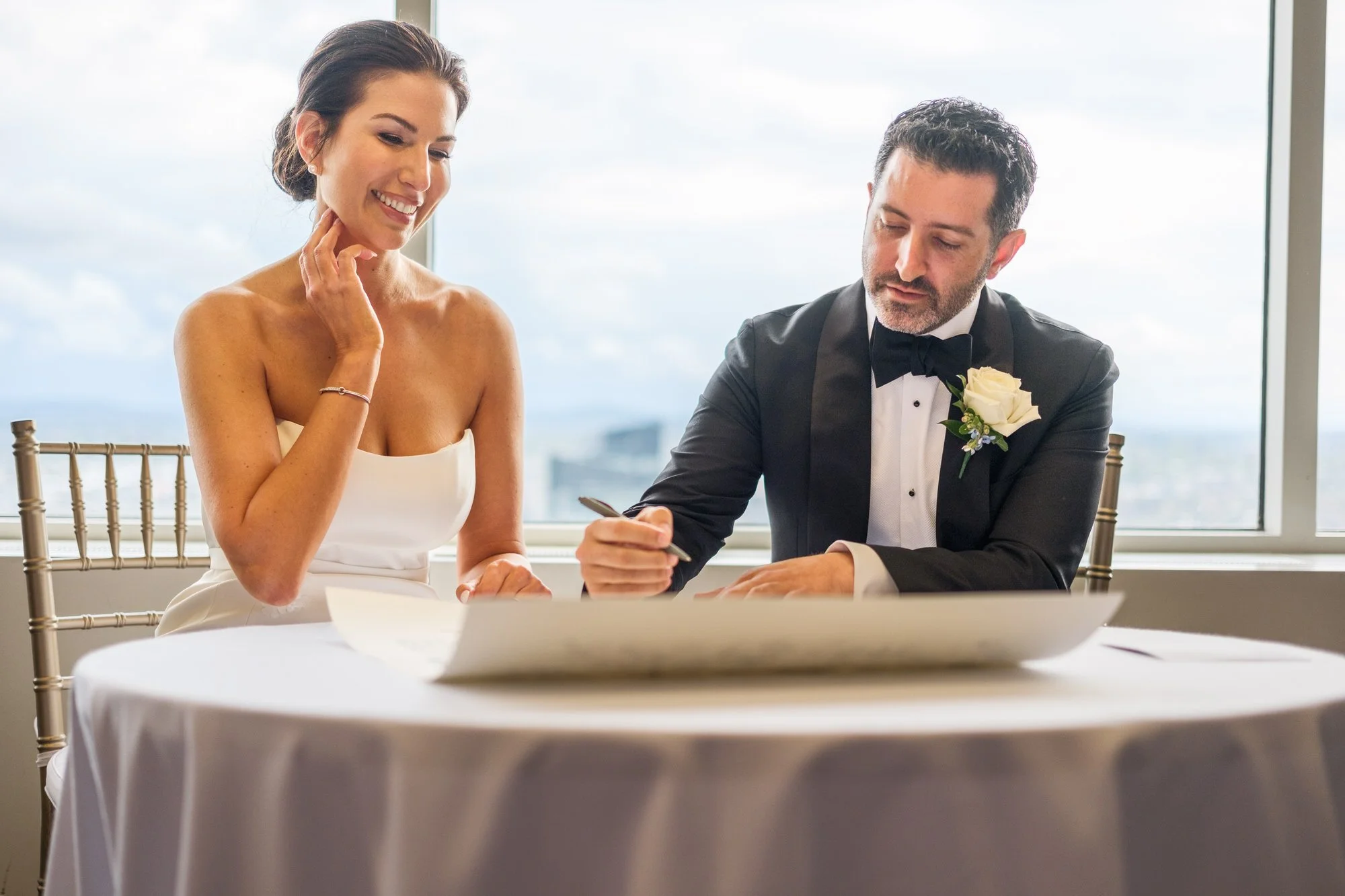 Groom signing the ketubah as bride looks on lovingly during the Jewish wedding ceremony at the UMass Club Boston