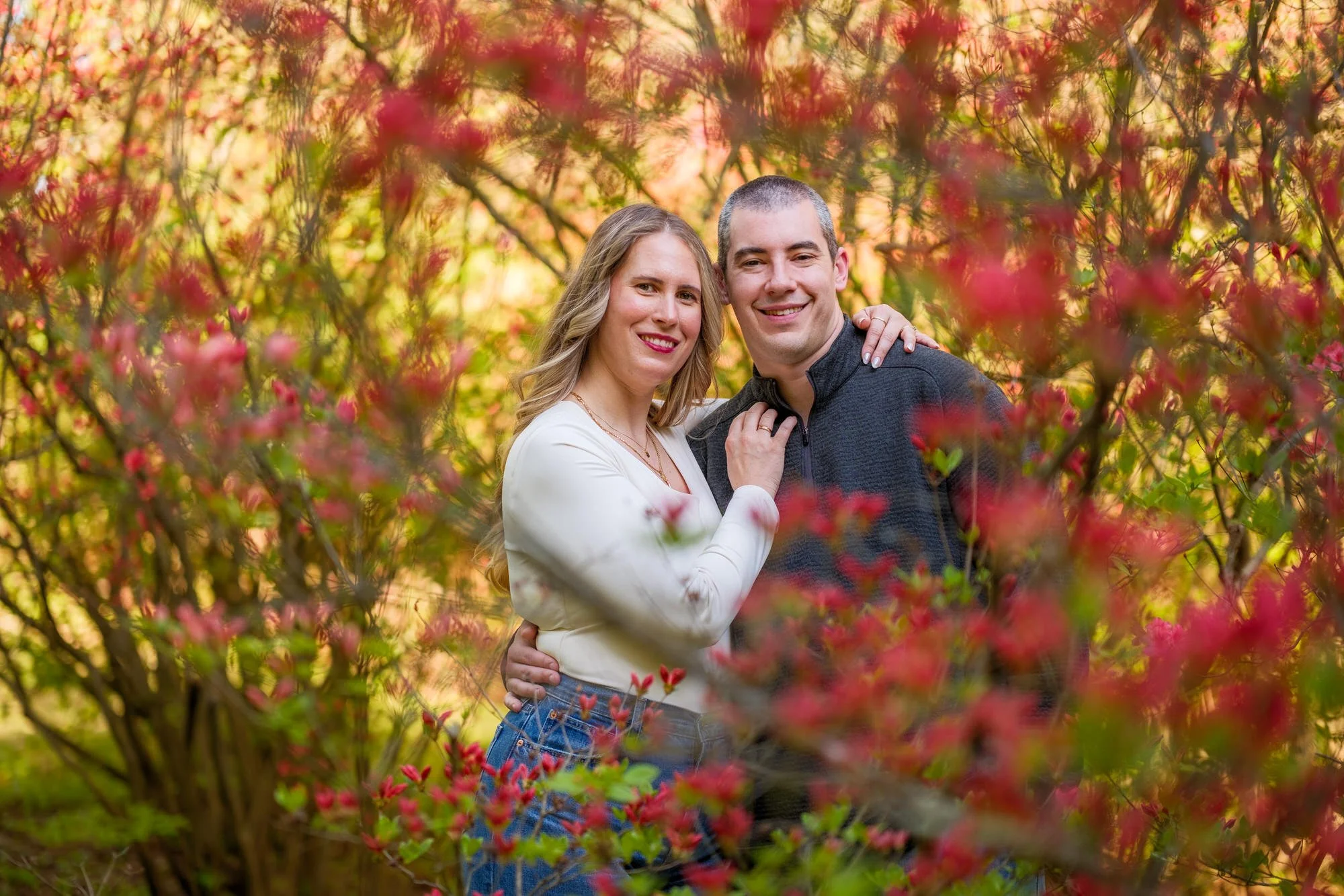 Couple embracing and smiling through vibrant red spring blooms at Maudslay State Park in Newburyport, MA