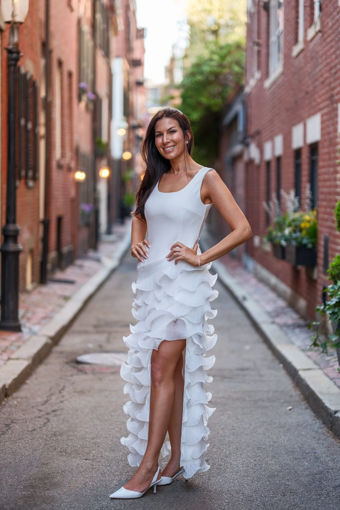 Bride Lauren posing solo in her white tiered ruffle gown on a narrow gaslit alley in Beacon Hill, Boston, with historic brick townhouses framing the scene on both sides