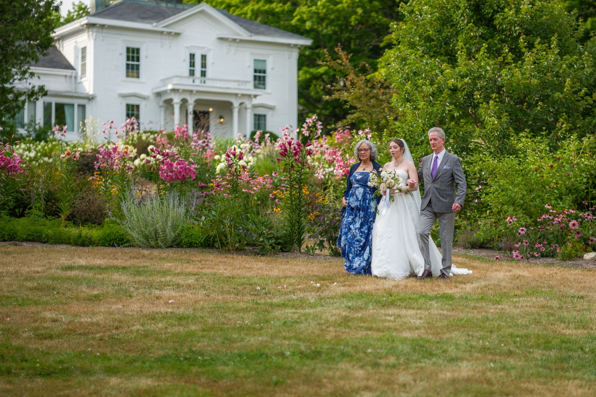 Bride walking toward the ceremony with family in the garden