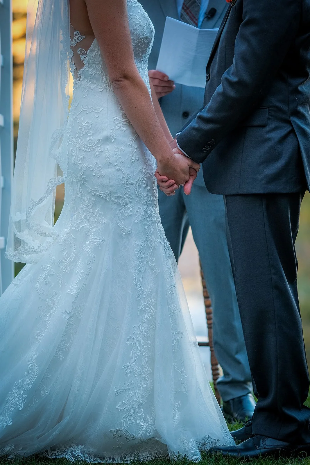 Bride and groom holding hands during a wedding ceremony, with an officiant in the background.