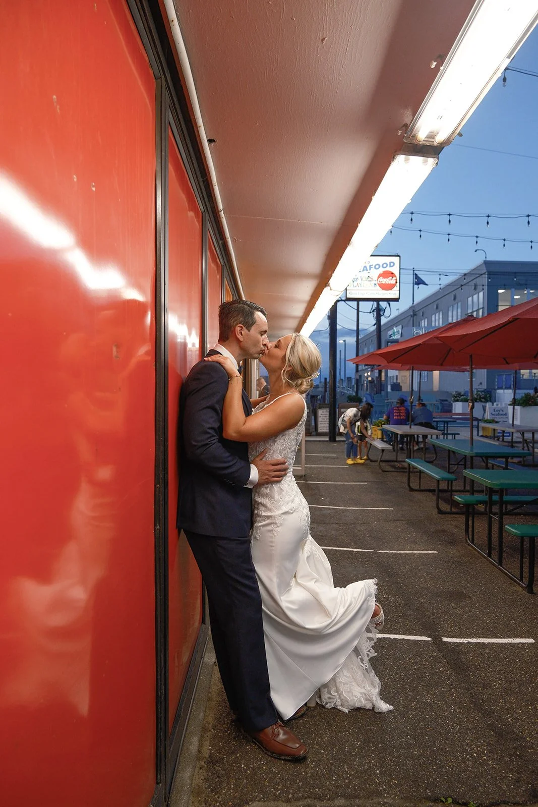 Bride and groom sharing a kiss against a bold red wall on the Salisbury Beach boardwalk near Blue Ocean Event Center