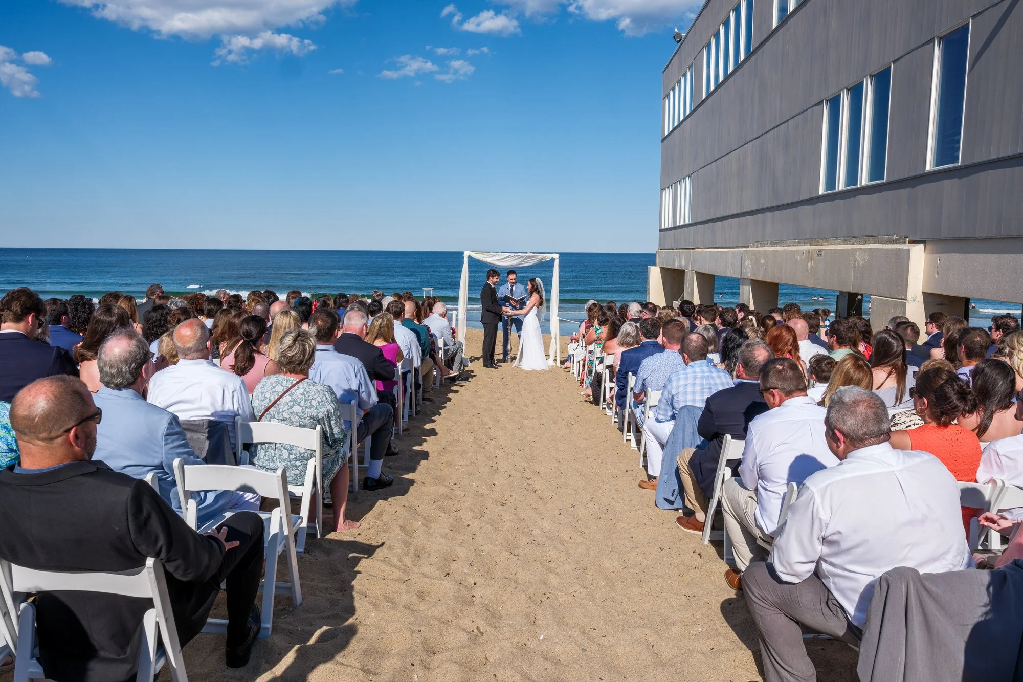 Wide view of a beach wedding ceremony beside Blue Ocean Event Center in Salisbury, MA.