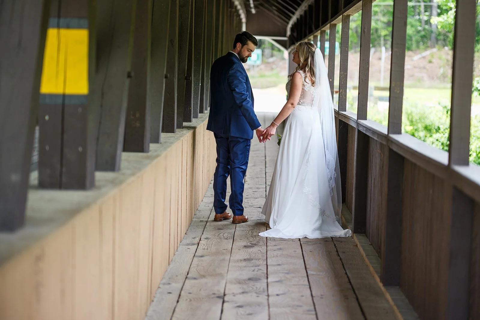 Bride and groom holding hands on a bridge, standing close and looking at each other, in a wedding photo.