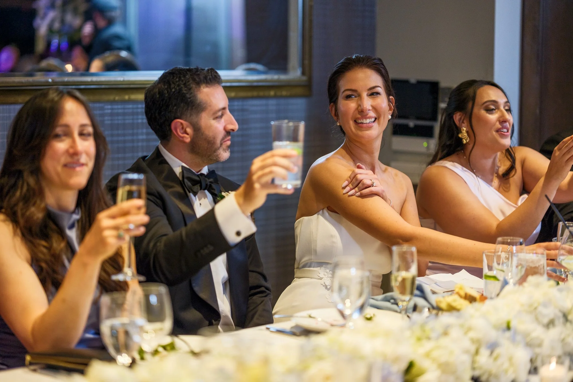 Bride smiling and groom raising a glass during wedding toasts at the UMass Club Boston reception