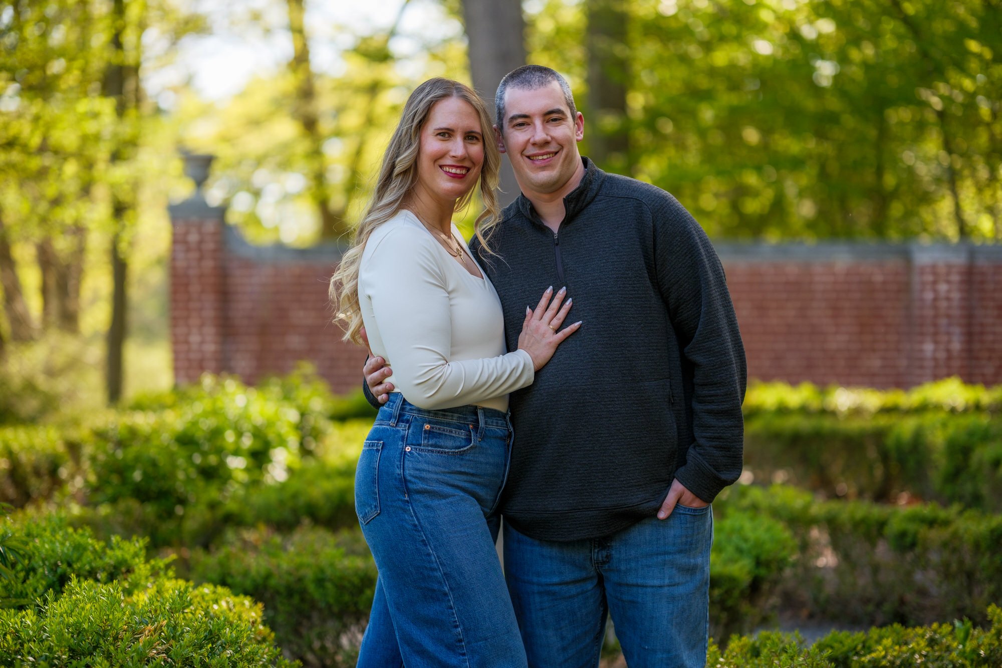 Engaged couple smiling together in front of the brick garden wall at Maudslay State Park in Newburyport, MA
