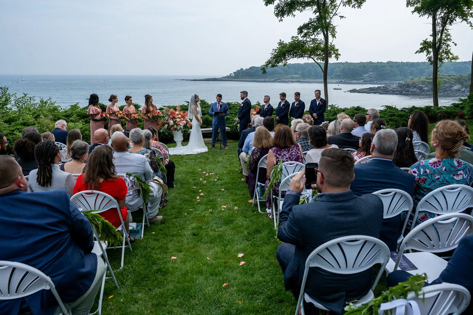 Wide aerial shot of outdoor wedding ceremony on a lawn overlooking the York Maine coastline