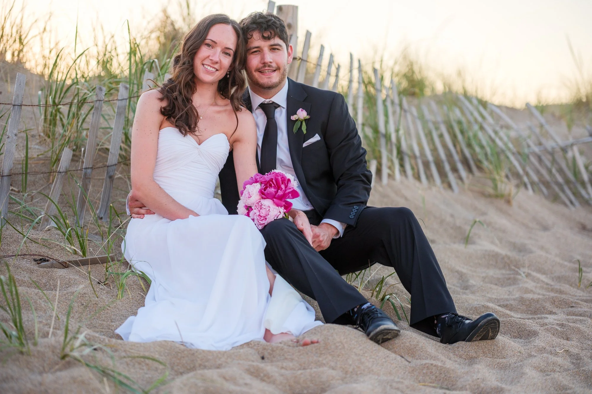 Bride and groom sitting in the dunes for wedding portraits near Blue Ocean Event Center.