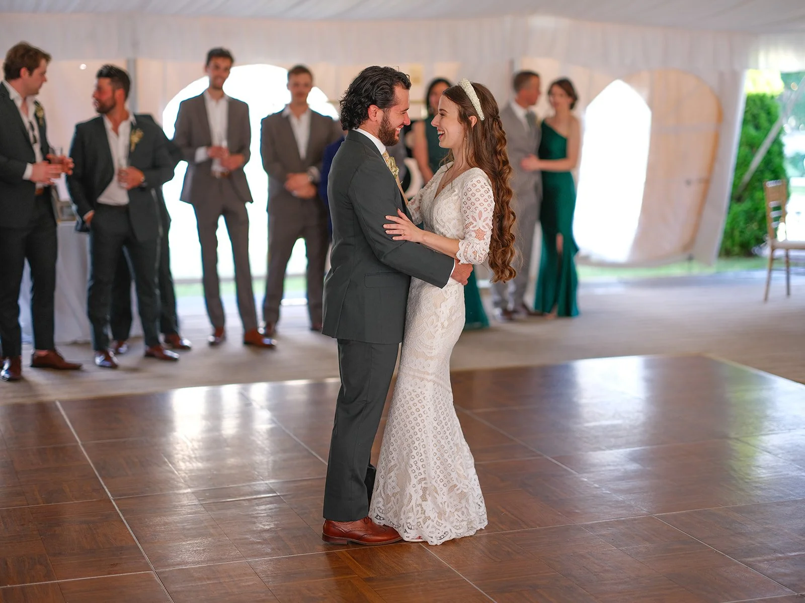 A bride and groom are dancing together in a reception hall, surrounded by friends and family.