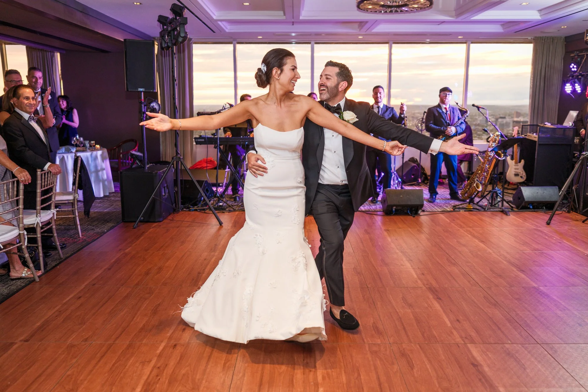 Bride and groom arms wide open laughing during their first dance at the UMass Club Boston reception with sunset backdrop
