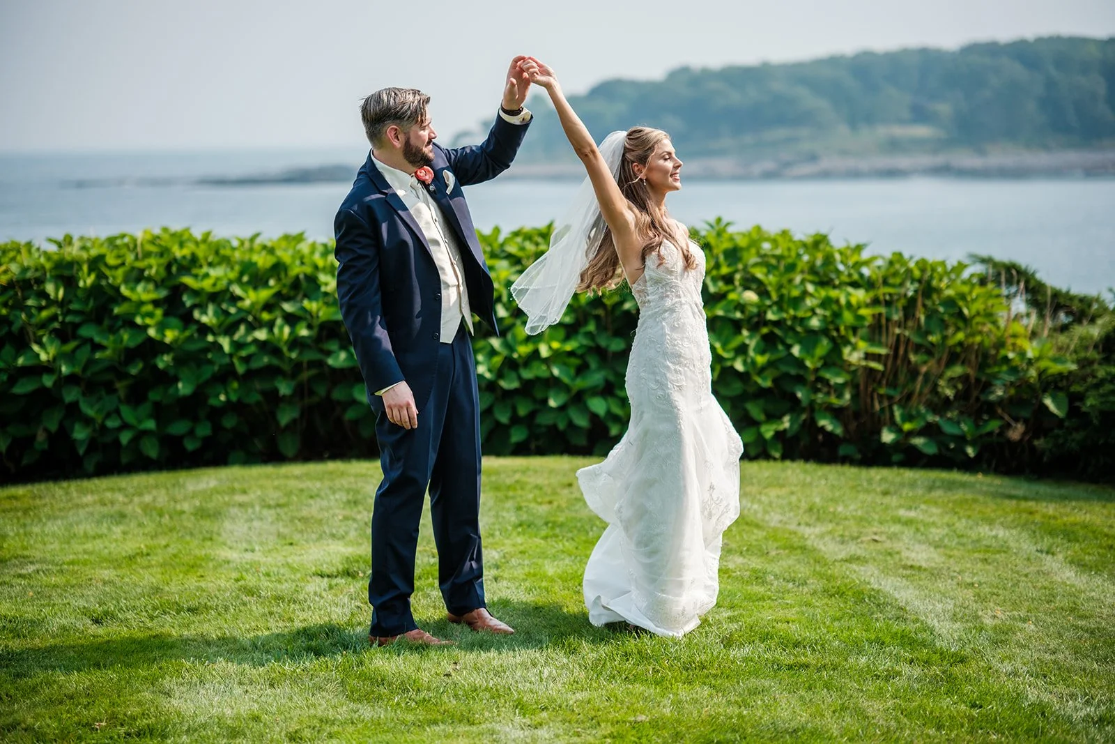 Groom twirling bride on green lawn with York Maine ocean and island views behind them