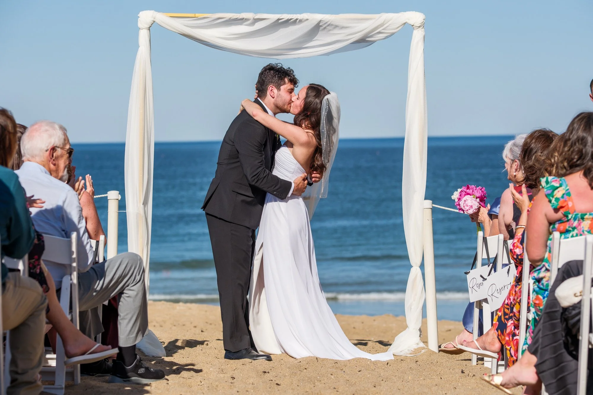 Bride and groom sharing their first kiss beneath a beach canopy at Blue Ocean Event Center.