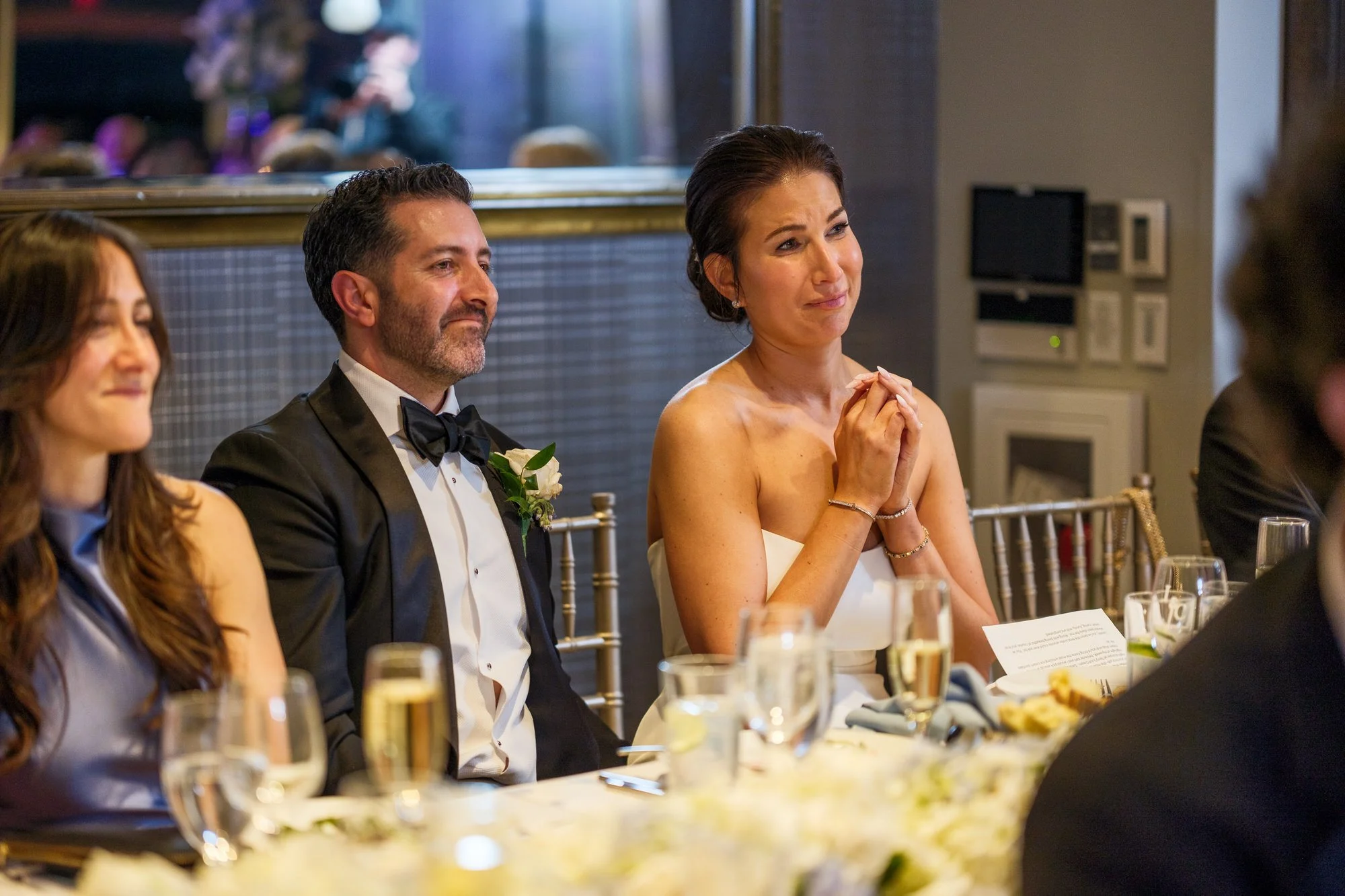Bride tearing up while groom watches with a smile during wedding toasts at the UMass Club Boston reception