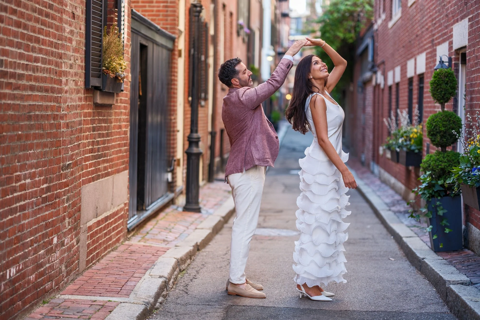 Charlie spinning Lauren in a graceful dance move on Acorn Street in Beacon Hill, her white ruffle dress swirling as she laughs and looks up, surrounded by Boston's historic brick architecture