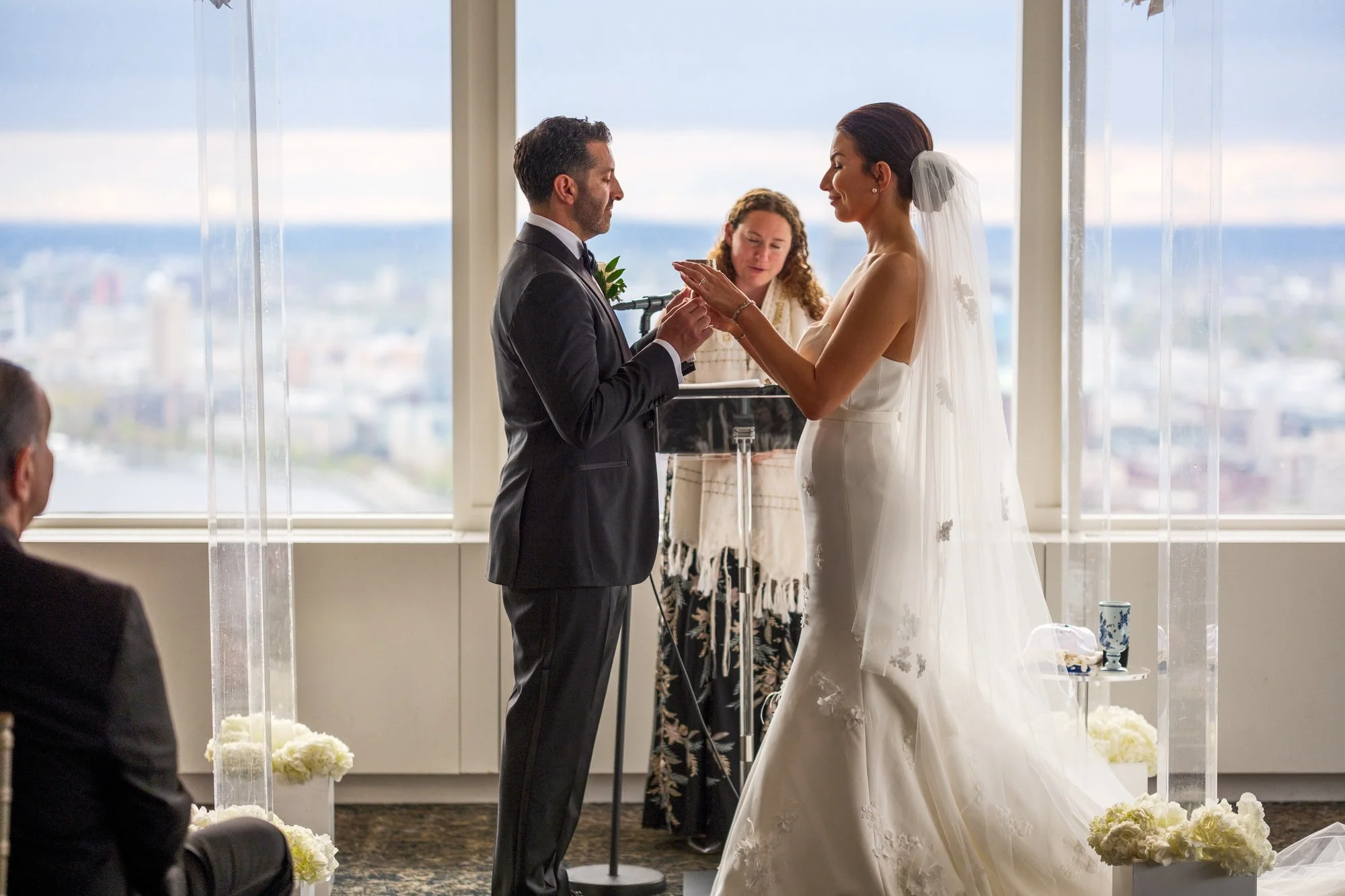 Bride placing wedding ring on groom's finger during ring exchange under the chuppah at the UMass Club Boston