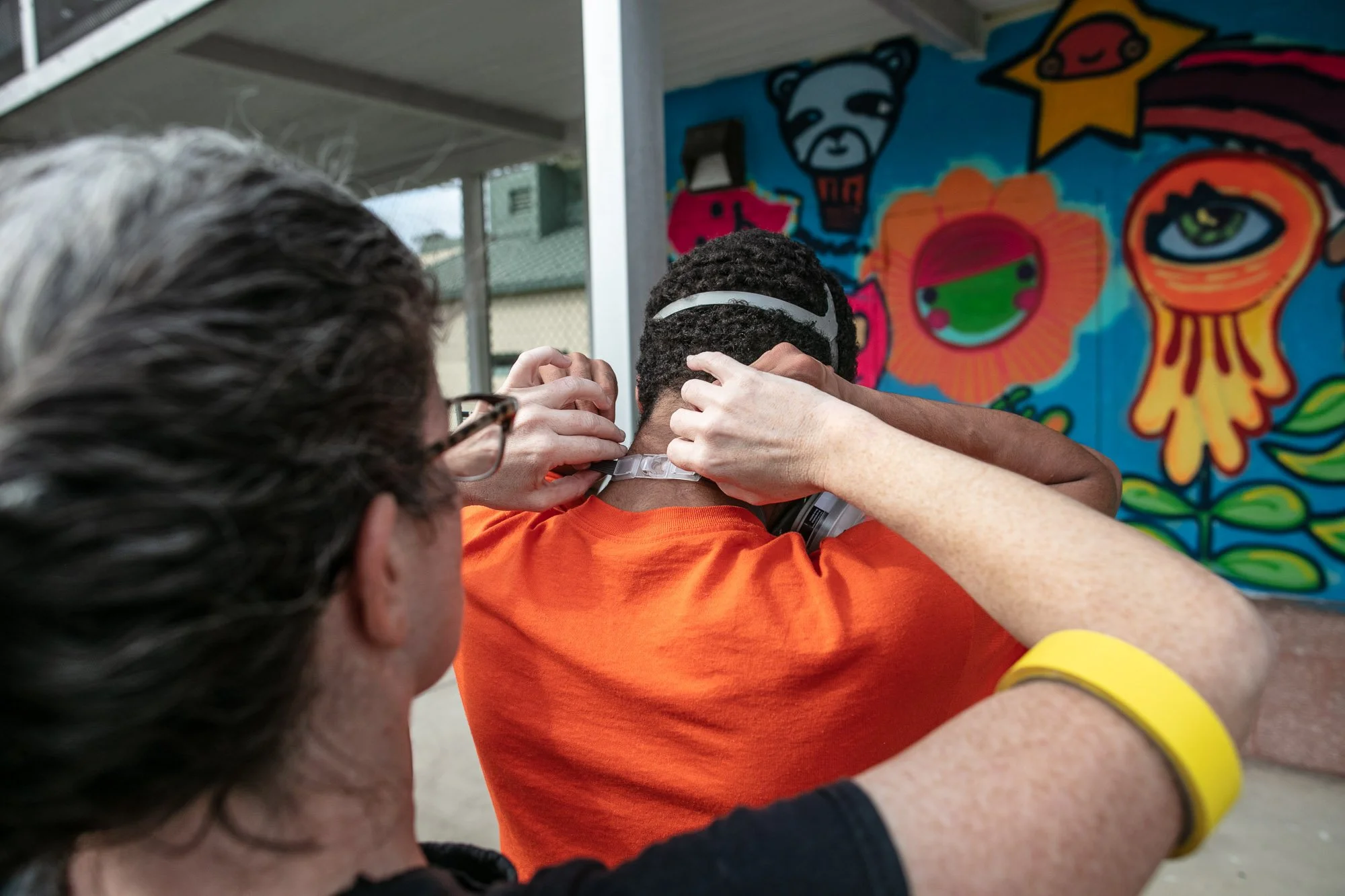 Closeup image of an adult helping a detained youth adjust their face mask before spray painting.