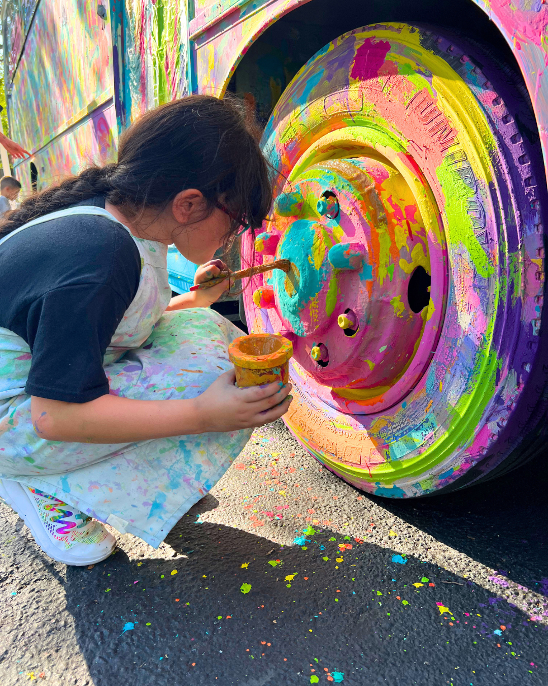 A child using a paintbrush to paint the tires of a bus