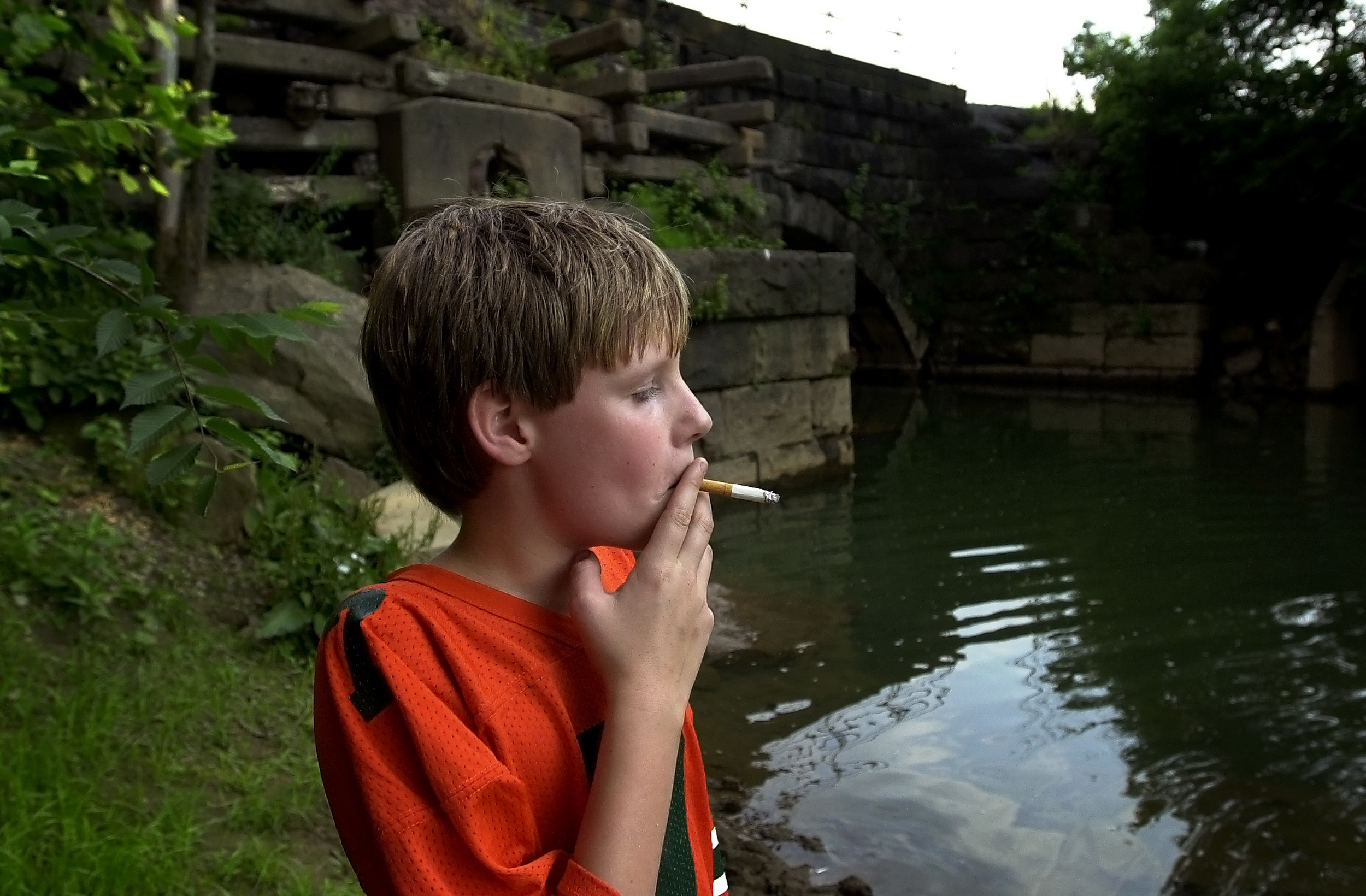 A boy smokes a cigarette as he hides along a stream in Tarentum, Pa.