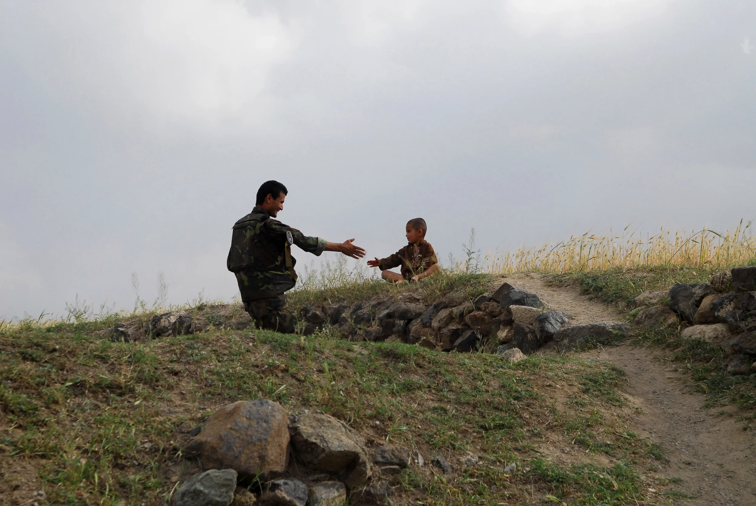 A police officer with the Afghanistan National Police (ANP) reaches out to shake the hand of a young child in a field while on patrol with the U.S. Army's 101st Airborne Divisions, in Legharah, a small village in the Khost Province of Afghanistan in May 2008.