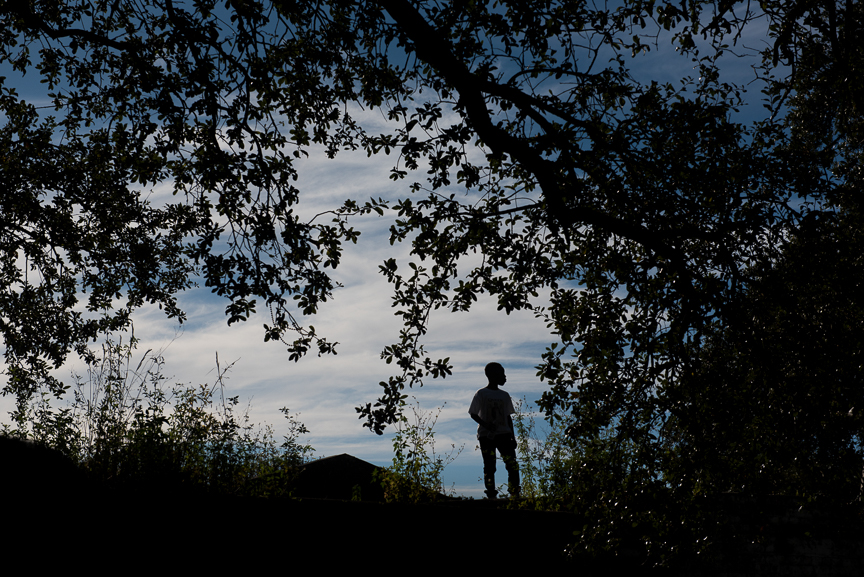 A young boy stands on top of a concrete wall at a cemetery as he watches a second line parade pass by in New Orleans. 