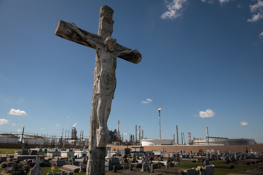 A crucifix stands in the Holy Rosary Cemetery in Killona, La., as the Dow Chemical Plant looms in the background. 
