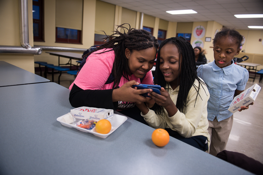 Monet Spencer looks at a game with Tya Carter, 10, as Aminyah Dooley, 5, looks on after an after-school tutoring session at Pittsburgh Miller PreK-5. Spencer earns about $100 every two weeks from the tutoring job. She pays $50 a month in rent.