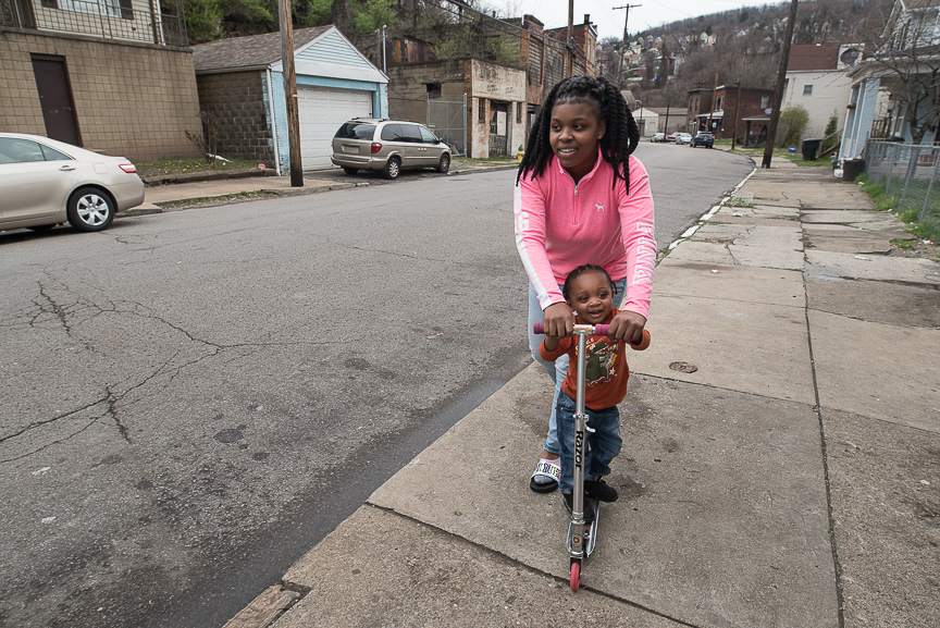 Dezmaire Baker, 17, helps her son, Dorian, 2, to ride a scooter along the sidewalk in front of their Braddock home on April 3, 2017.