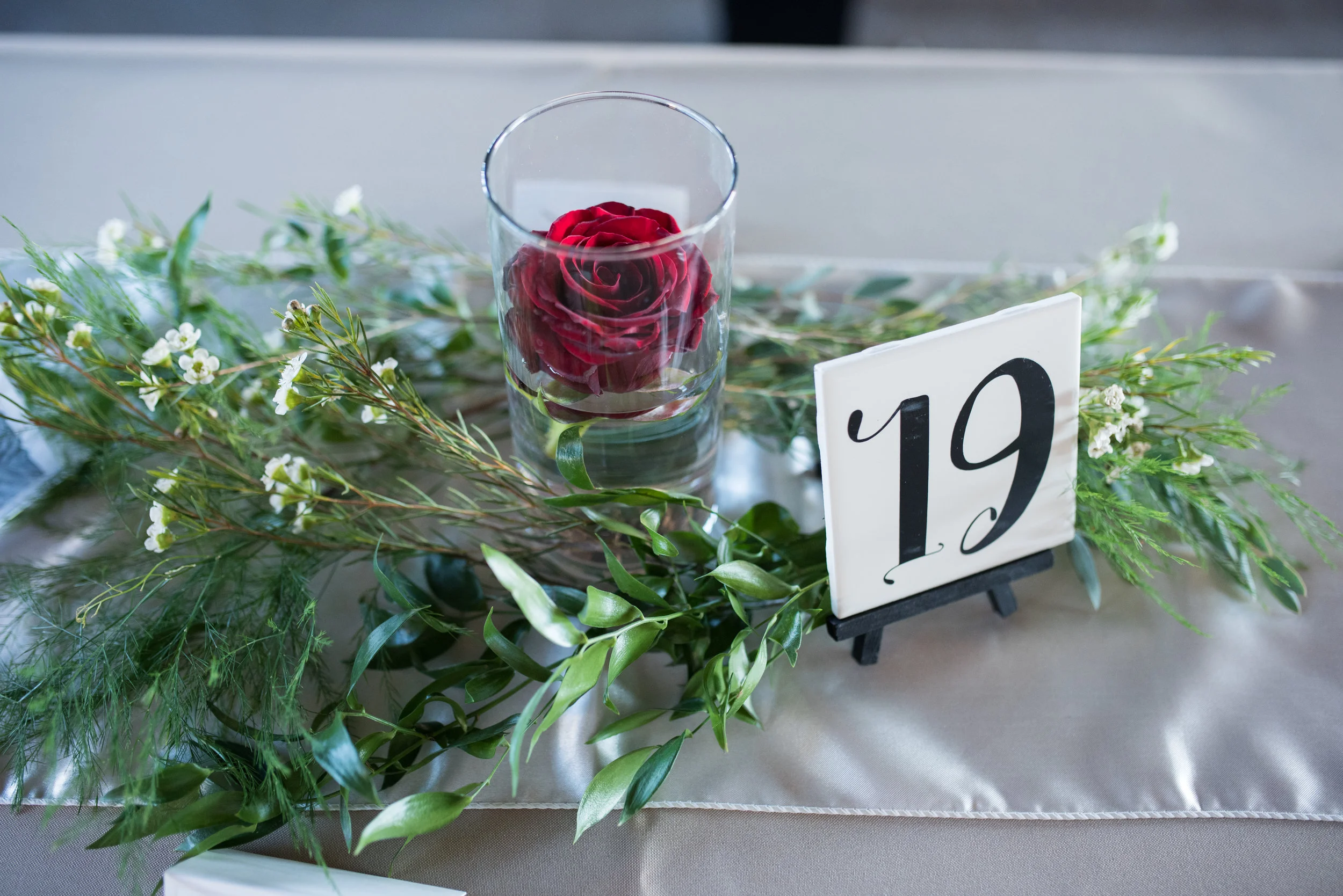 The reception was softened with floating roses surrounded by sprigs of green and white flowers. The head table had a beautiful garland and their last name in wood blocks, topped off with custom wedding rings behind the head table.