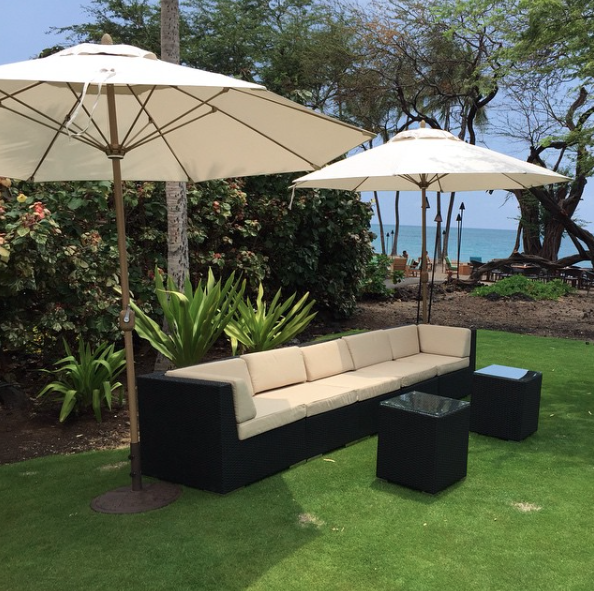 Black Wicker Sectional accompanied by two End Tables, and two Market Umbrellas.