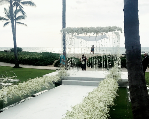 Custom white walkway and staging with white carpeting for ceremony at Four Seasons Hualalai palm grove. Flowers Grace Flowers Hawaii