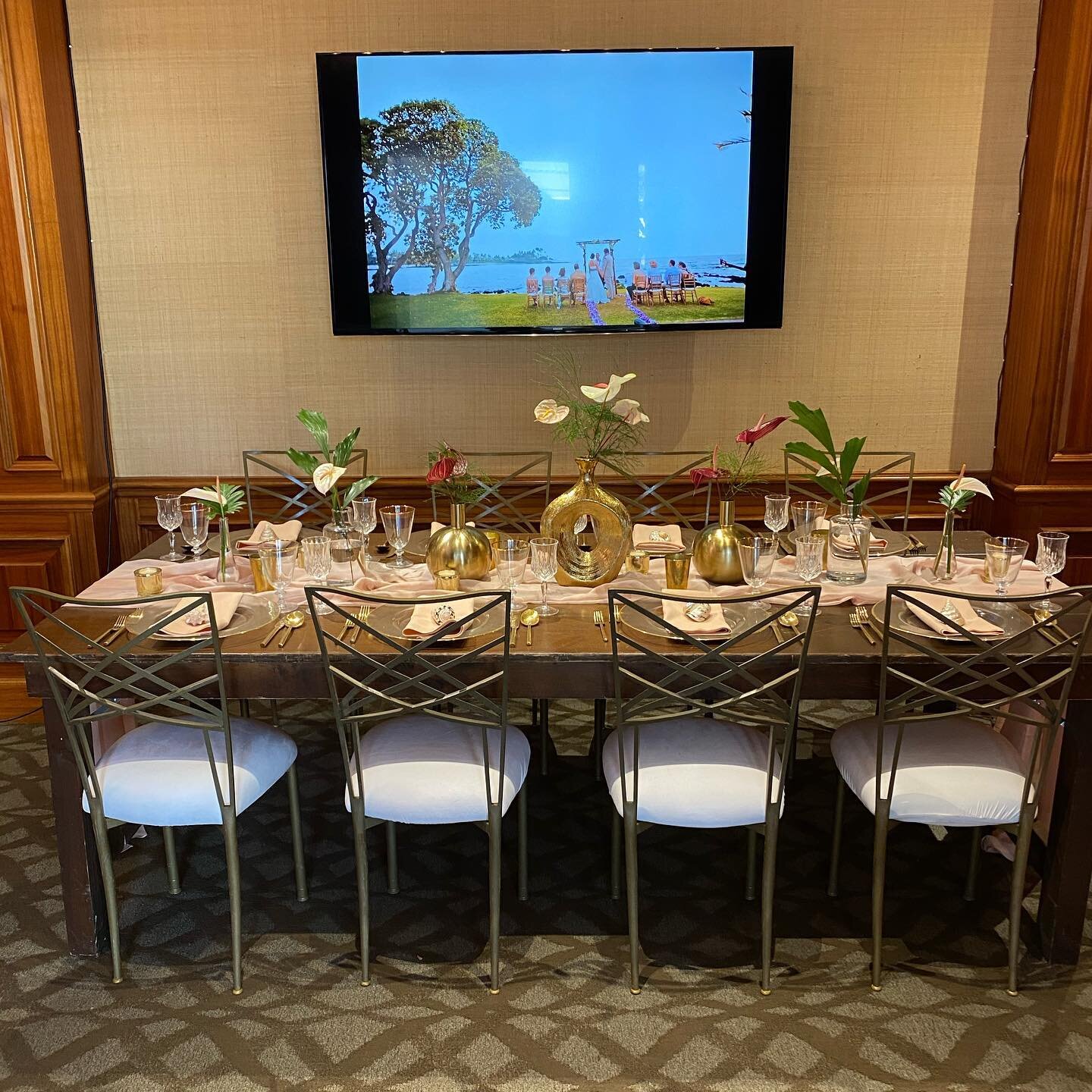 @fairmontorchid wedding show room with our gold fan fare chairs with white pads, farm table, gold rimmed glass chargers, gold rim multi purpose glasses, gold flatware, crystal water goblets, pink rug, white leather loveseat, dark wood chiavari chairs