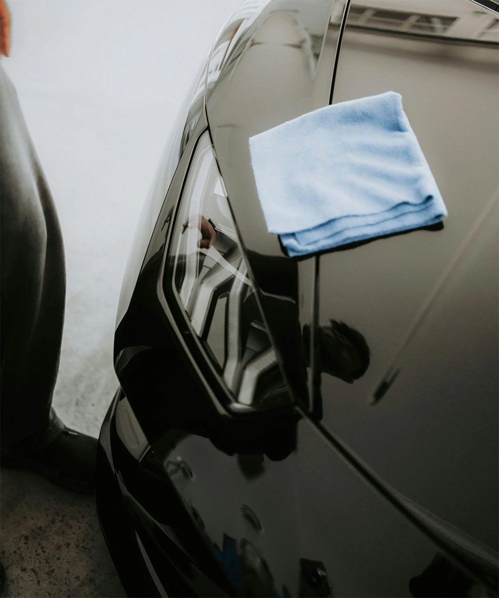 Close-up of a black vehicle being polished during a mobile exterior detailing service.