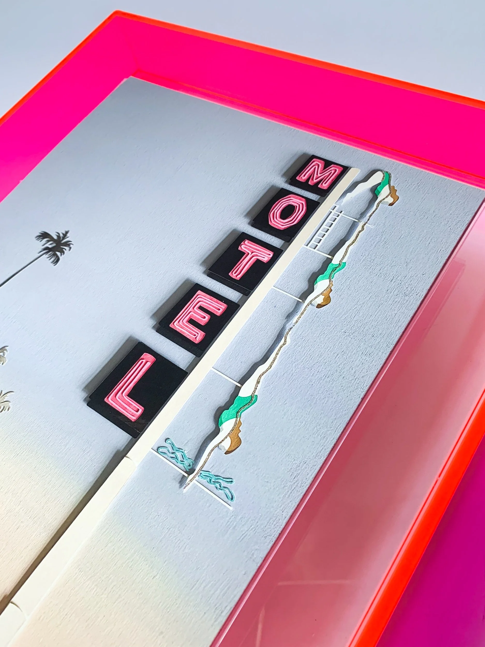 Print of a neon motel sign in a neon pink frame, with a diving lady icon and MOTEL lettering
