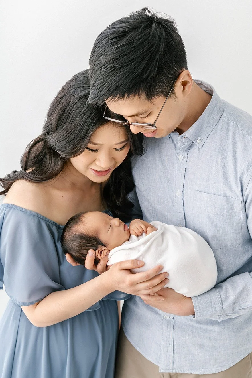 Asian mother and father wearing soft blue waradrobe hold newborn baby in natural and tender embrace