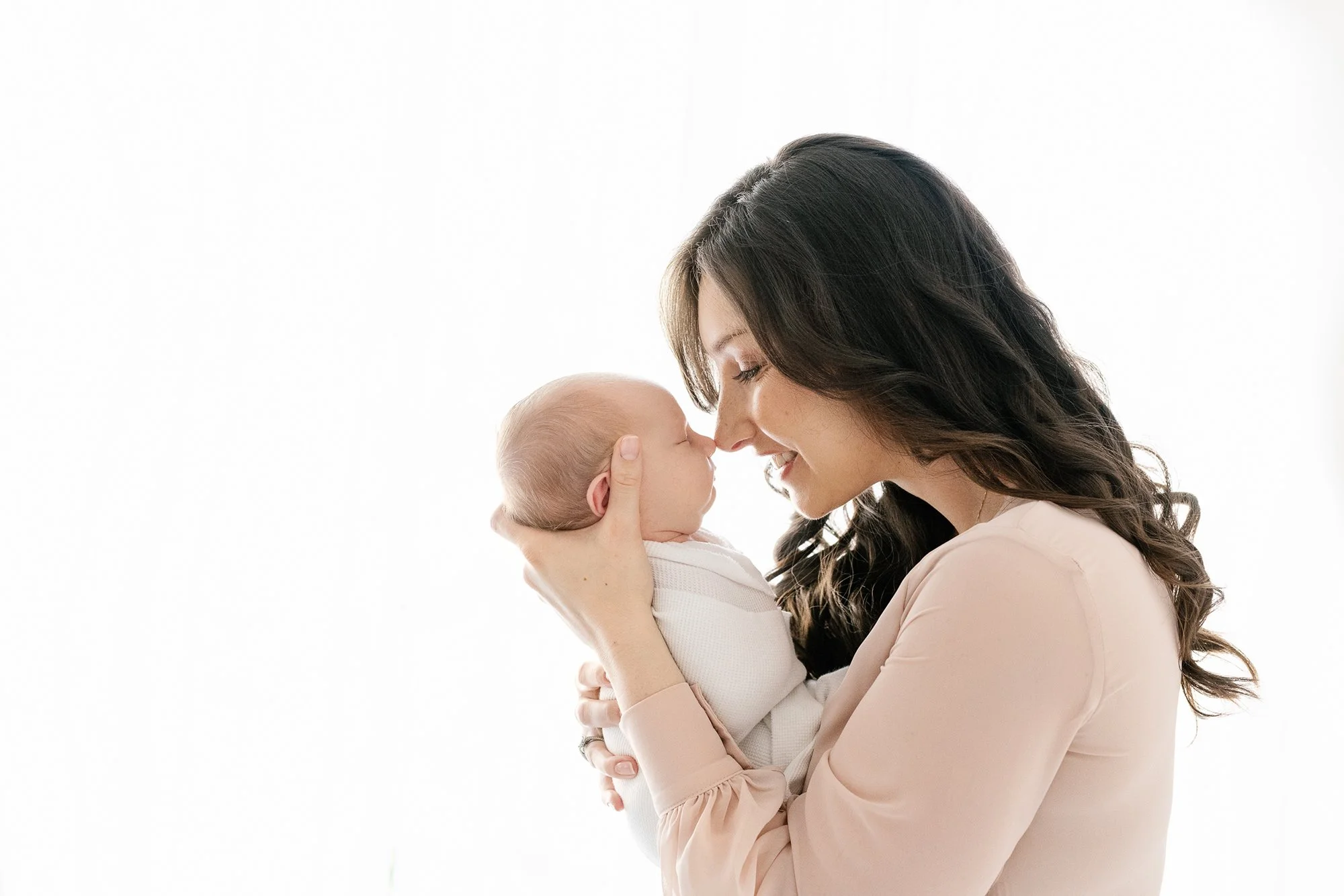 Smiling new mother in pink dress holds newborn baby in NJ photo studio