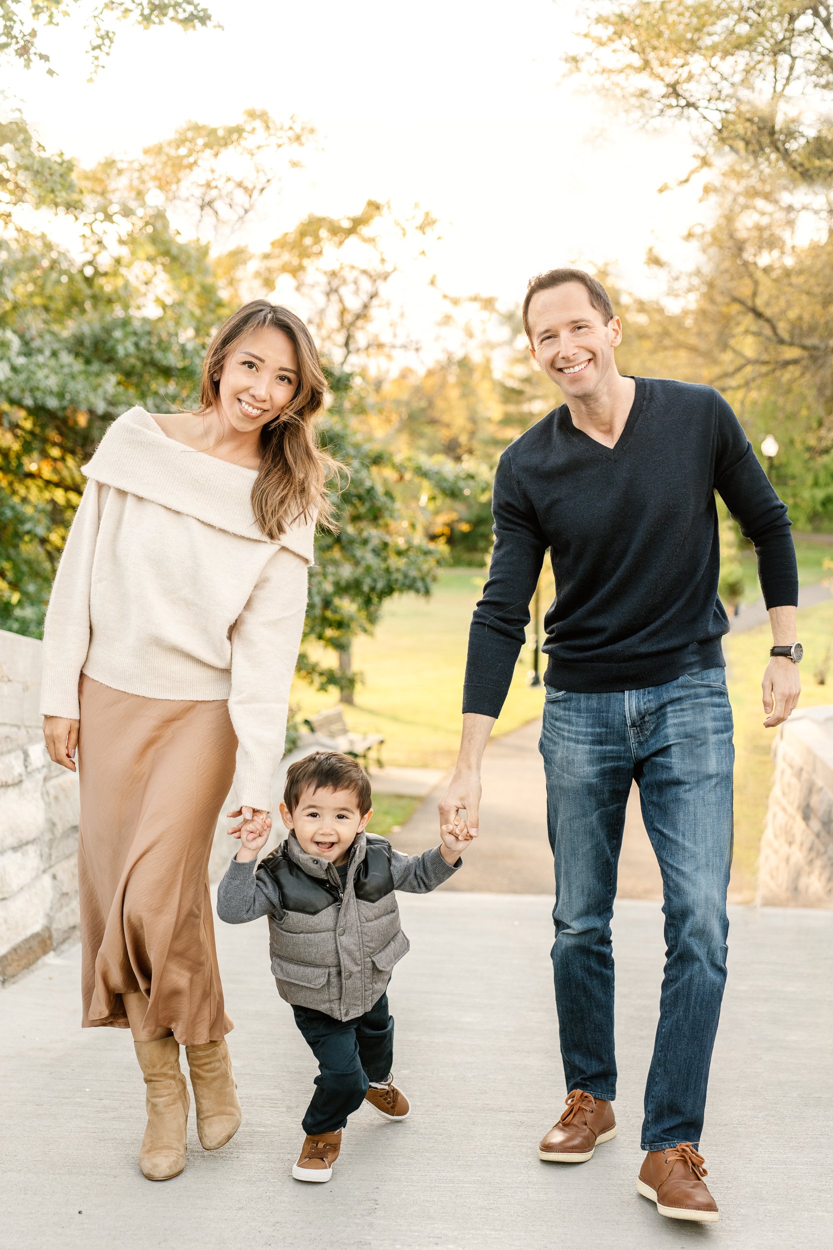  In Northern New Jersey at Verona Park, a mother in a tan skirt and a father in a black sweater help their young son walk by holding his hands by Nicole Hawkins Photography. sweaters for pictures black man sweater cream sweater #nicolehawkinsphotogra