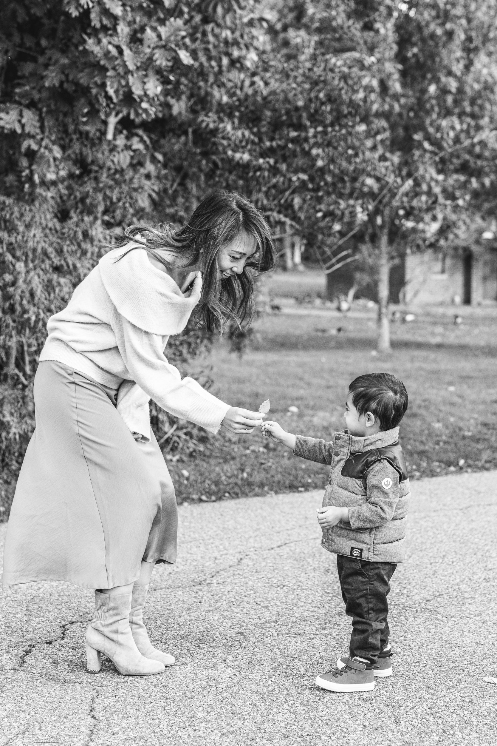  A mother crouches over and accepts a leaf from her young son during a family session with Nicole Hawkins Photography in New Jersey. mother and son candid family photo moments mommy pictures toddler boy #nicolehawkinsphotography #nicolehawkinsfamilie
