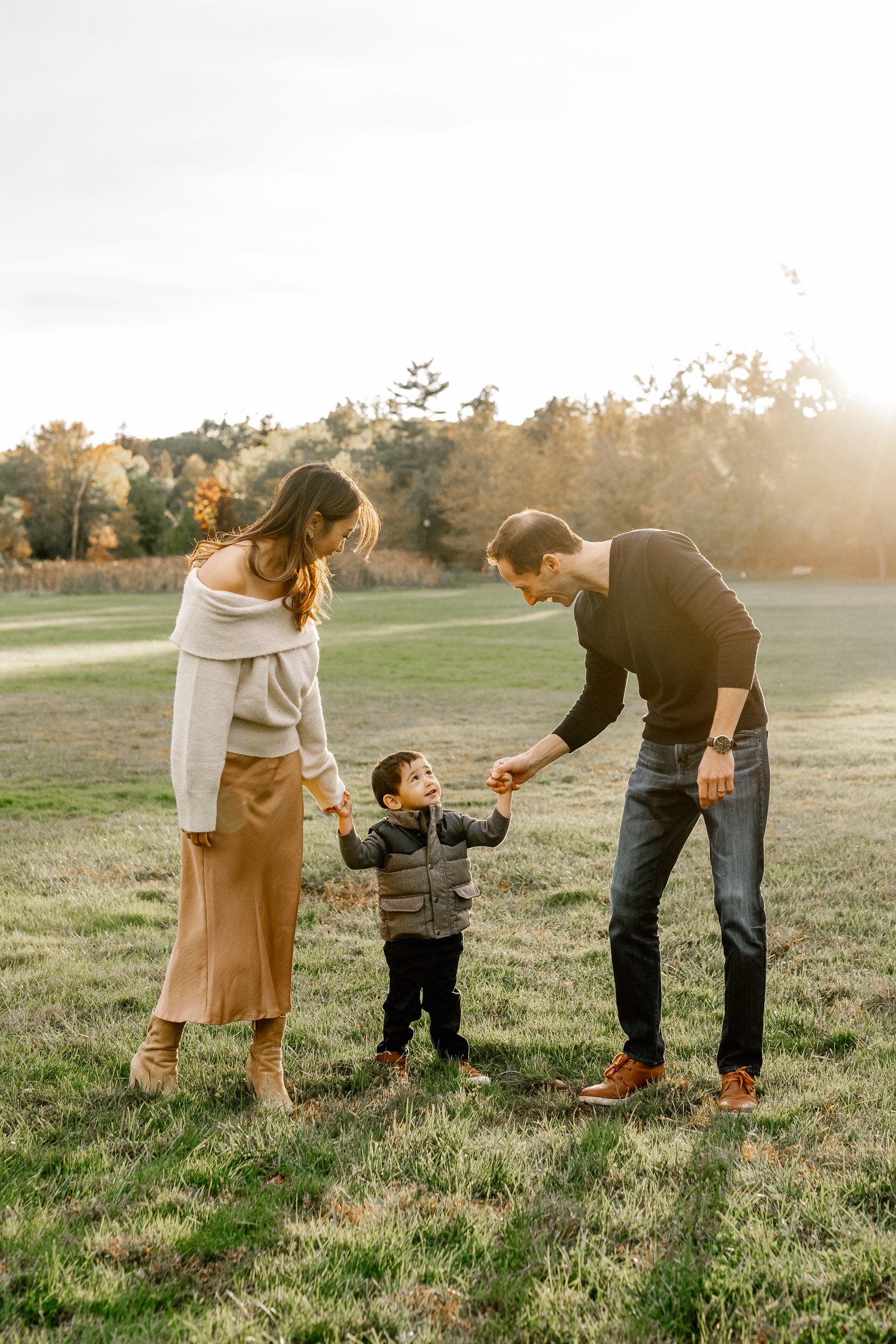  In New Jersey, a mother and father grab onto their son's hands and walk with him next to the fall foliage by Nicole Hawkins Photography. NJ fall family photos parents with child one-child family pictures&nbsp; #nicolehawkinsphotography #nicolehawkin