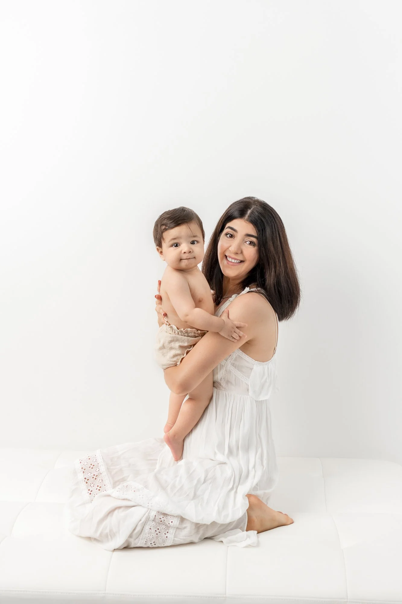  New Jersey baby photographer Nicole Hawkins Photography captures a mother in a white dress kneeling down and holding her baby boy in her arms. Neutral outfits for family portraits classic family photo ideas #nicolehawkinsphotography #nicolehawkinsba
