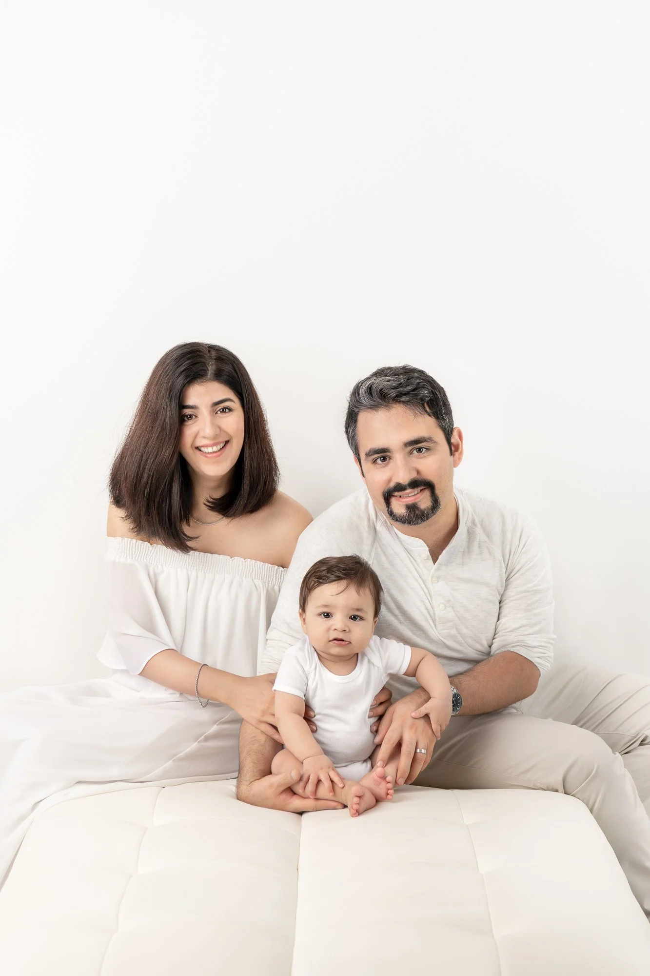  At a bright studio in New Jersey, a family takes a photo with a white modern classic vibe by Nicole Hawkins Photography. all-white family outfits white wall studio baby boy in white baby photography #nicolehawkinsphotography #nicolehawkinsbabies #ne