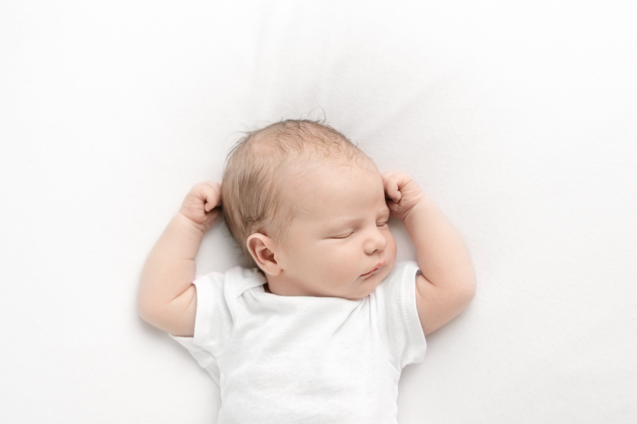  A newborn photographer in New Jersey captures a sleeping baby with both arms up by her head during a studio newborn session with Nicole Hawkins Photography. sleeping baby baby on a bed white studio inspiration flexing baby #nicolehawkinsphotography 