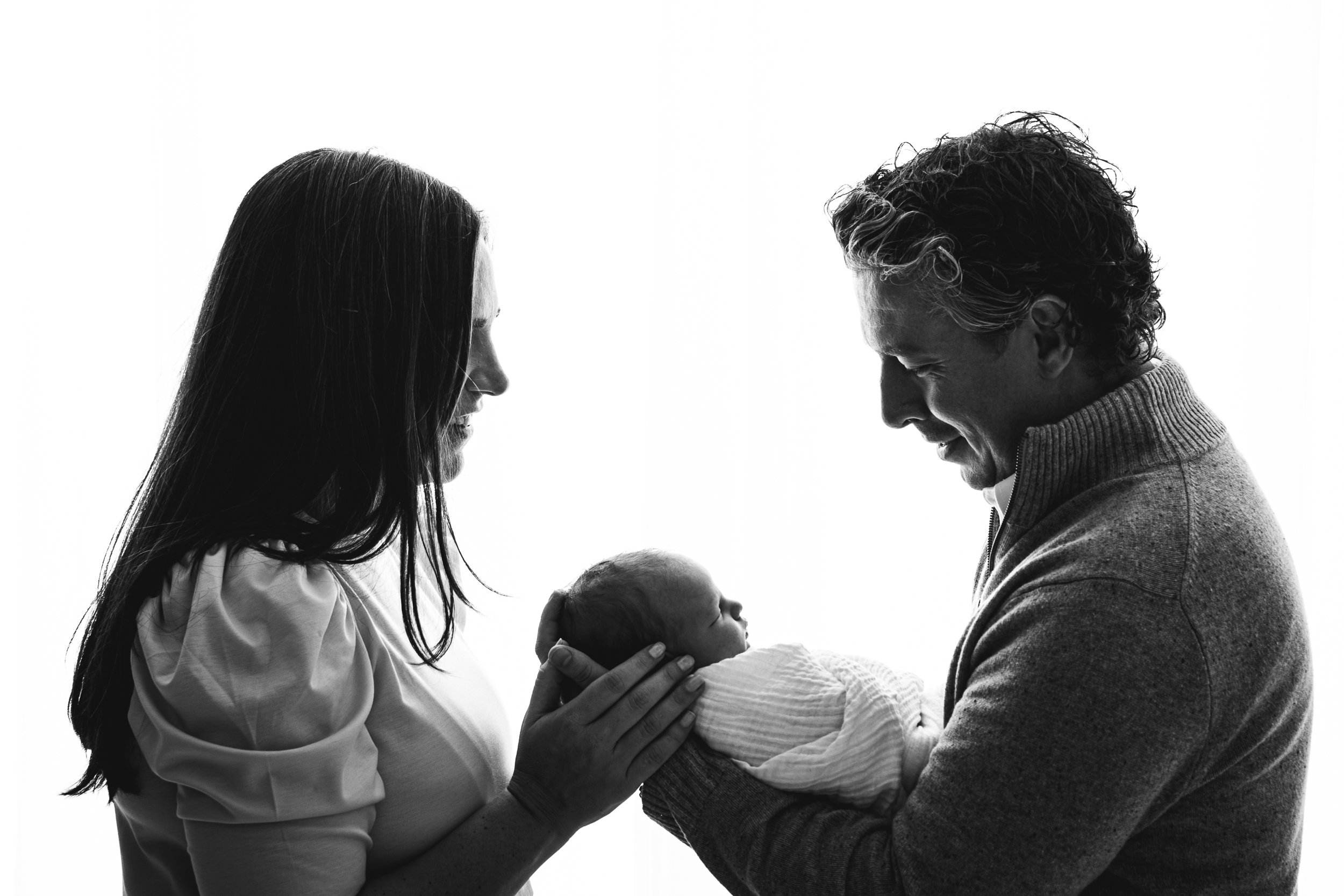  Nicole Hawkins Photography captures a stunning black and white silhouette of a father and mother looking down at their brand new baby in a studio in New Jersey. mother and father silhouette mother and father holding baby girl #nicolehawkinsphotograp