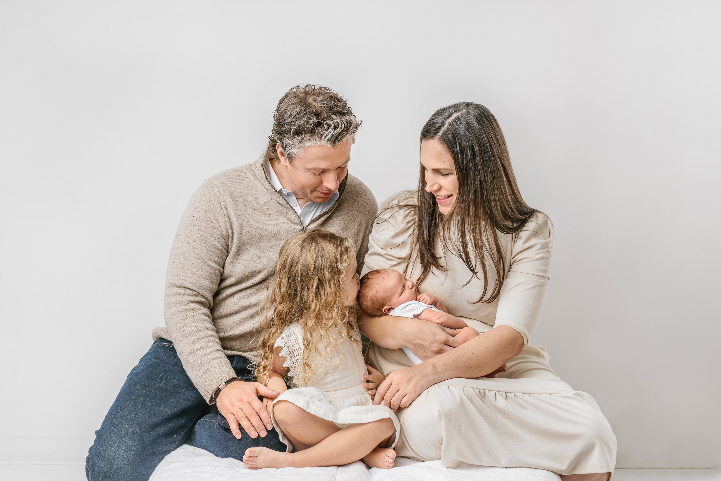  A new family of four all smile down at the new baby in the mother's arms in New Jersey during a studio session with Nicole Hawkins Photography. newborn family sessions new family of four mother with two little girls #nicolehawkinsphotography #nicole