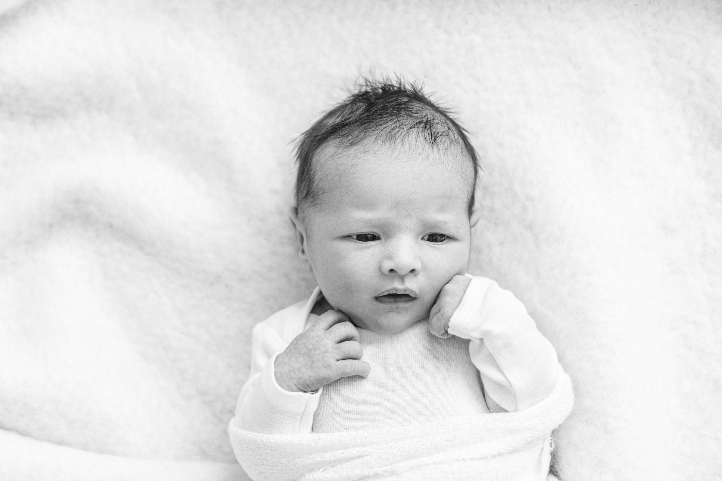  Baby girl with eyes wide open and fists next to her face captured by Nicole Hawkins Photography a professional photographer in Hoboken, New Jersey. baby girl baby with eyes open hands next to face baby on bed #nicolehawkinsphotography #nicolehawkins